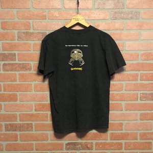 Könnte beinhalten: Schwarzes T-Shirt mit einem Grafikdruck einer Person mit Helm und dem Text "Ein Erlebnis wie kein anderes. GameWorks"