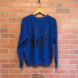 Puede incluir: Una sudadera azul real con un estampado gráfico negro de una ciudad y el texto "Castle Point is Pride".