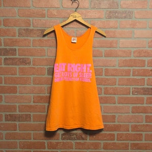 May include: Orange sleeveless tank top with the text "EAT RIGHT. GET LOTS OF SLEEP. DRINK PLENTY OF FLUIDS." printed in pink.