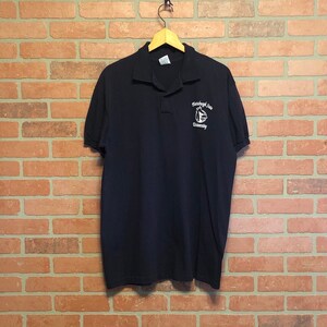 Può includere: Una polo blu scuro con un logo ricamato bianco che dice "Randolph-Macon University".