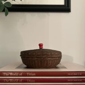 May include: A woven brown basket with a red knob on top sits atop a stack of books. The books are titled "The World of Titian", "The World of Dürer", and "The World of Giotto". The books are part of the Time-Life Library of Art series.