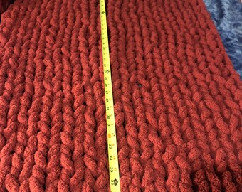 May include: A large, red knitted throw blanket with a yellow measuring tape along the side. The tape measures 40 inches.