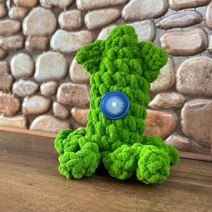 May include: Green crocheted octopus plush toy with a blue button for an eye.