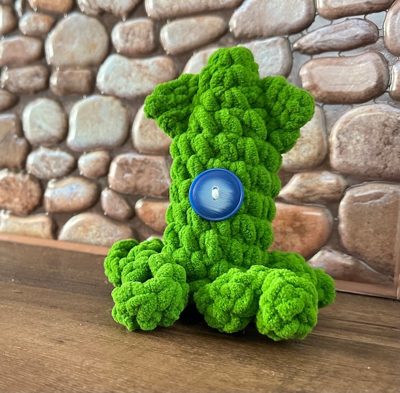May include: Green crocheted octopus plush toy with a blue button for an eye.