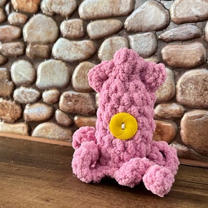 May include: A pink crocheted octopus with a yellow button for an eye.