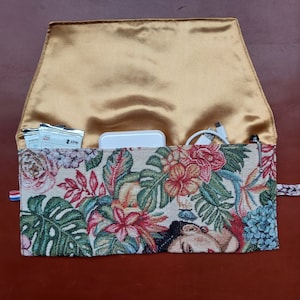 May include: A floral patterned zippered pouch with a gold satin lining. The pouch is open and contains a white power bank, two small white packages, and a white charging cable.