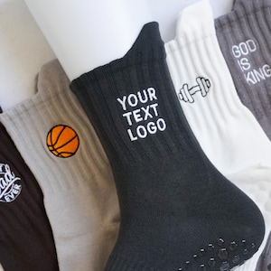 Könnte beinhalten: Verschiedene Crew-Socken in verschiedenen Farben, darunter Schwarz, Grau und Weiß. Einige Socken haben gestickte Designs wie einen Basketball, eine Hantel und den Text "YOUR TEXT LOGO" und "GOD IS KING".