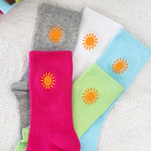 Puede incluir: Cinco pares de calcetines con soles bordados. Los calcetines son de varios colores, incluyendo rosa, verde, azul, blanco y gris.