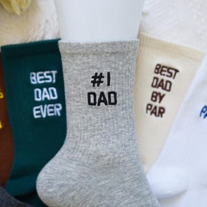 May include: A collection of crew socks in various colors, each embroidered with a message for Father's Day. The socks include the phrases "Best Dad Ever," "#1 Dad," and "Best Dad by Par" in contrasting thread colors.