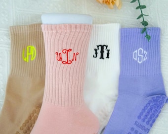 May include: Four pairs of crew socks in tan, pink, white, and lavender. Each sock features a different embroidered monogram in coordinating colors. The socks have ribbed cuffs and non-slip grips on the soles, ideal for sports or casual wear.
