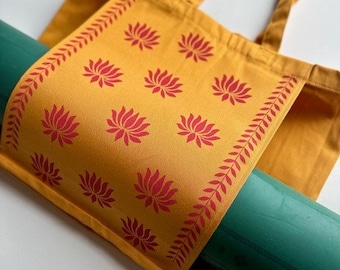May include: A yellow tote bag with red lotus flower designs and a green yoga mat inside. The bag has a long strap for carrying over the shoulder.