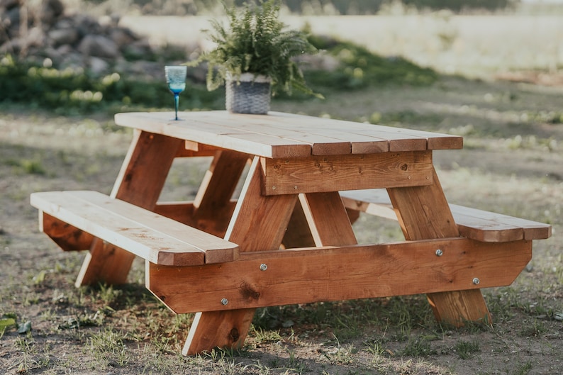 May include: A wooden picnic table with two benches, made of natural wood with a reddish-brown stain. A blue glass sits on the table.