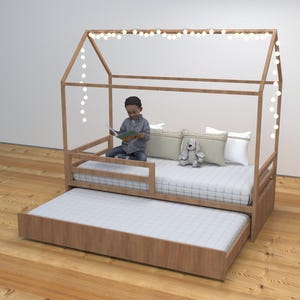 Puede incluir: Una cama de madera con dosel en forma de casa y una cama auxiliar extraíble. Un niño está sentado en la cama leyendo un libro. La cama está decorada con luces de cadena.