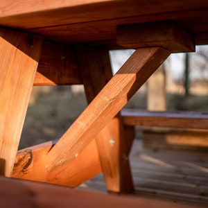 May include: Close-up of the wooden support beams of a picnic table. The beams are made of natural wood and are stained a rich brown color. The beams are joined together with screws and form a sturdy and stable base for the table.