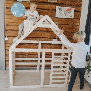 May include: Two children are playing in a wooden playhouse with a ladder and a roof. The playhouse is made of natural wood and has a simple design. The children are wearing casual clothes and are having fun.