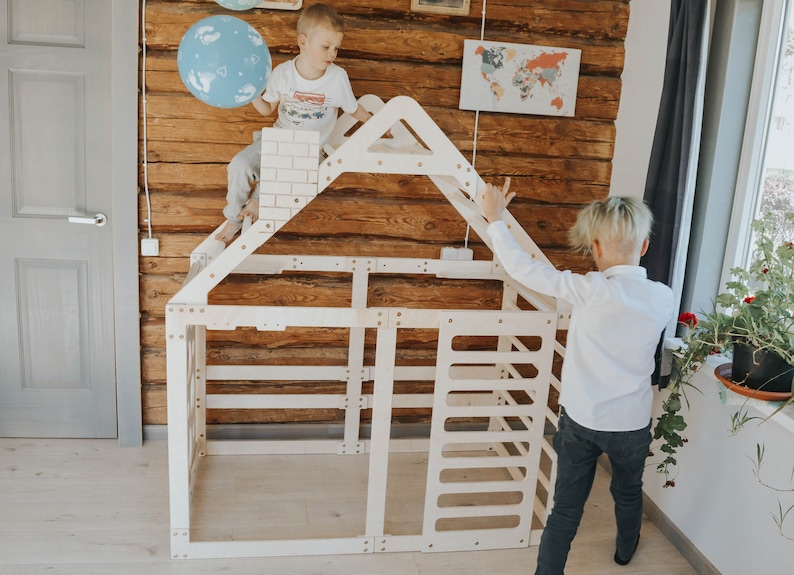 May include: Two children are playing in a wooden playhouse with a ladder and a roof. The playhouse is made of natural wood and has a simple design. The children are wearing casual clothes and are having fun.