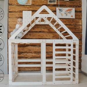 May include: White wooden playhouse with a climbing wall, ladder, and a small chimney. The playhouse is designed for children aged 1-8 and is made in Europe. The playhouse is eco-friendly and helps build muscle strength.