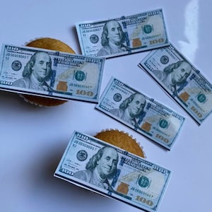 Könnte beinhalten: Vier Cupcakes, die mit essbaren Bildern von 100-Dollar-Scheinen verziert sind. Jeder Cupcake hat einen grünen Schein mit einem Porträt von Benjamin Franklin und dem Text "THE UNITED STATES OF AMERICA" und "ONE HUNDRED DOLLARS".