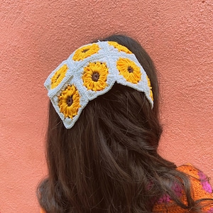 Puede incluir: Una diadema blanca de ganchillo con dise&ntilde;os de girasoles amarillos. La diadema est&aacute; puesta en una persona con el pelo largo y casta&ntilde;o.
