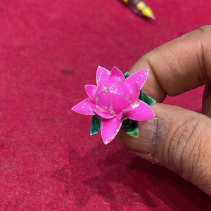May include: A pink origami lotus flower with green leaves. The flower is made of paper and has a delicate, intricate design.
