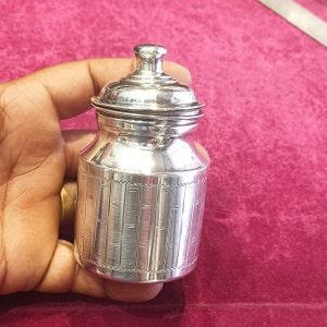 May include: A silver container with a lid, featuring a bamboo-like pattern. The container is small and has a rounded shape.