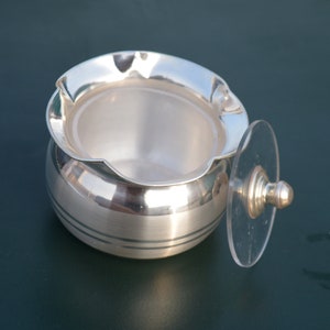 May include: Silver sugar bowl with a clear glass lid and a silver knob. The bowl has a fluted rim and two silver bands around the body.