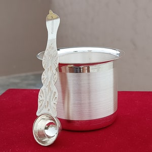 May include: A silver cup and a silver spoon with intricate designs. The cup is cylindrical and has a wide rim. The spoon has a long handle with a rounded bowl.