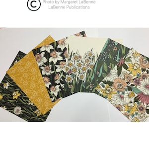 May include: A collection of floral patterned cards, featuring daffodils and other botanical designs. The cards display a variety of colors, including yellow, black, white, and pink. The cards are arranged in a fan shape, showcasing the different patterns.