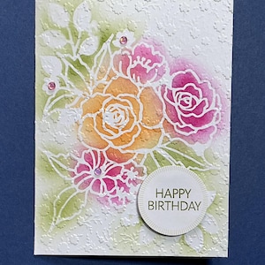 May include: A handmade birthday card featuring a bouquet of watercolor roses in shades of orange and pink. The card has a white embossed background with a floral pattern and the words "HAPPY BIRTHDAY" in a circular label.
