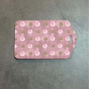 May include: A pink luggage tag with a pattern of pink roses and gold dots. The tag has a rectangular shape with rounded corners and a small cutout for attachment. The design is repeated across the surface.