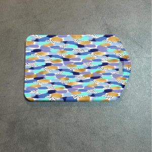 May include: Rectangular cutting board with a handle, featuring a colorful abstract pattern. The design includes blue, gold, purple, and black brushstrokes with white polka dots. The board is made of a durable material.
