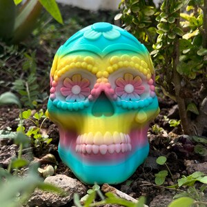 May include: A colorful sugar skull with pink, yellow, blue, and white flowers on the eyes. The skull is made of a smooth, glossy material.