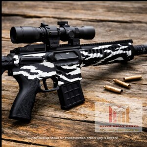 May include: A black and white rifle with a scope, featuring a zebra stripe pattern. The rifle is lying on a wooden surface with three bullets. The text "HIGH HEAT VINYL" and "We cut it, you cook it" is visible.