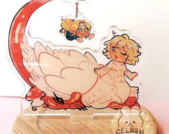 May include: A clear acrylic stand with a cartoon illustration of a character riding a swan-like creature with a red tail. The stand is on a round wooden base. A small mushroom is also included in the design. The text "CELISH" is visible.