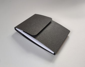 Matt black pocket notebook with magnet-closure. Refillable handmade wipe-clean cover with A7 notepad, plain pages.