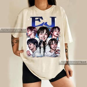 May include: Cream-colored t-shirt featuring a graphic of a musical artist with the letters "EJ" in blue. The graphic includes multiple images of the artist. The text "THEPRIDEOFVIETNAM" is printed on the shirt.
