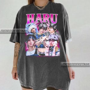 May include: Dark gray t-shirt featuring a graphic of a group of people with the word "HARU" in pink and purple. The text "THEPRIDEOFVIETNAM" is printed on the shirt. The shirt has short sleeves and a crew neck.
