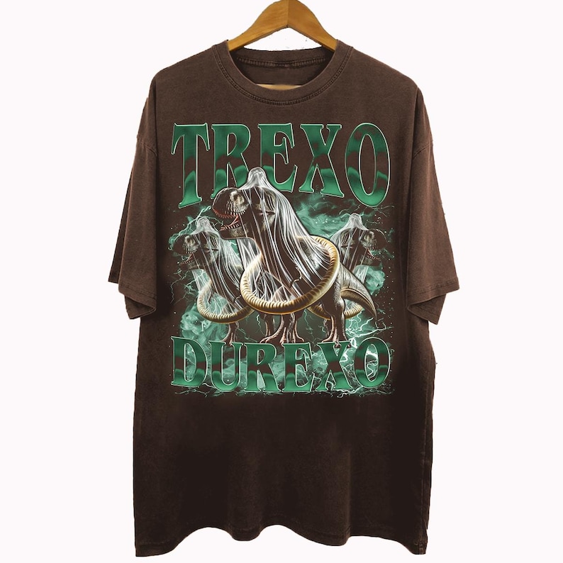 K&ouml;nnte beinhalten: Braunes T-Shirt mit einem Grafikdesign, das einen Dinosaurier mit Kondom zeigt, mit den Worten "TREXO DUREXO" in gr&uuml;nen Blockbuchstaben. Das Design hat einen Vintage- und Used-Look.