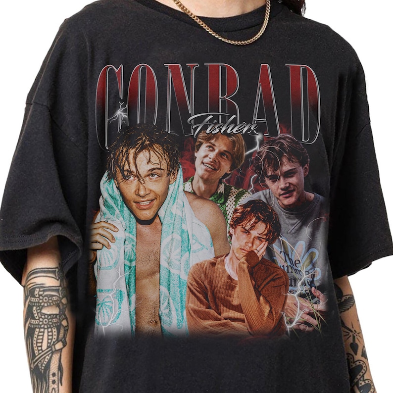 May include: Black t-shirt featuring a vintage-style graphic of four young men. The word "CONRAD" is printed in red above the images, with "Fishers" in white script below. The design has a faded, distressed look.