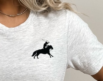 May include: A heather grey short-sleeved t-shirt with a black silhouette of a person riding a horse on the left chest. The text "ASH" is visible in the bottom right corner of the image.