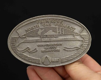 May include: A silver metal commemorative coin with the text "Primrose North Gas Project 300 Hours Construction Safety Milestone AEC".