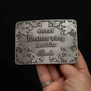 May include: Silver-toned metal belt buckle with an ornate design and the text "Great Western Tong Service Brooks".