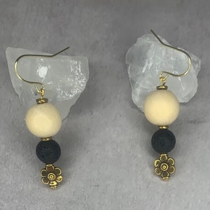 May include: A pair of gold earrings with a white bead, a black bead, and a gold flower charm.