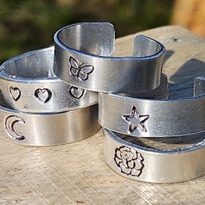 May include: Five silver rings with different designs. The rings feature a crescent moon, three hearts, a butterfly, a star, and a rose.