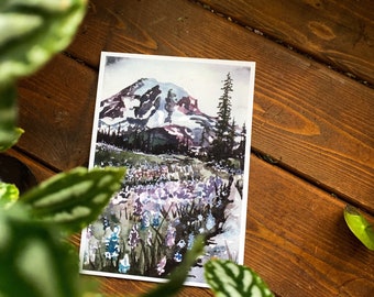 Può includere: Dipinto ad acquerello di una catena montuosa con una cima innevata, circondata da un campo di fiori selvatici viola. Il dipinto ha un'atmosfera morbida e sognante ed è incorniciato da un bordo bianco.