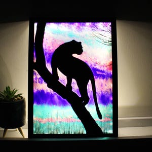 Może przedstawiać: Czarna sylwetka pantery siedzącej na gałęzi na tle kolorowego tła w odcieniach fioletu, różu i błękitu. Tło ma efekt akwarelowy.