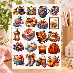 May include: A sticker sheet featuring autumn-themed illustrations including a pot with oranges, a mug in a knit cosy, a plaid scarf, a pumpkin with buttons, a lantern, a blanket, a book, cinnamon rolls, slippers, a candle, a jumper, and mittens.