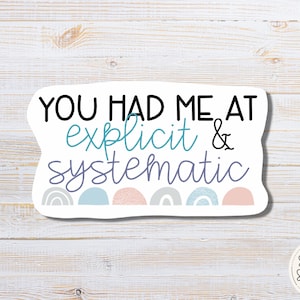 May include: White sticker with the text "You had me at explicit & systematic" in black. The text is surrounded by a row of colorful abstract shapes.