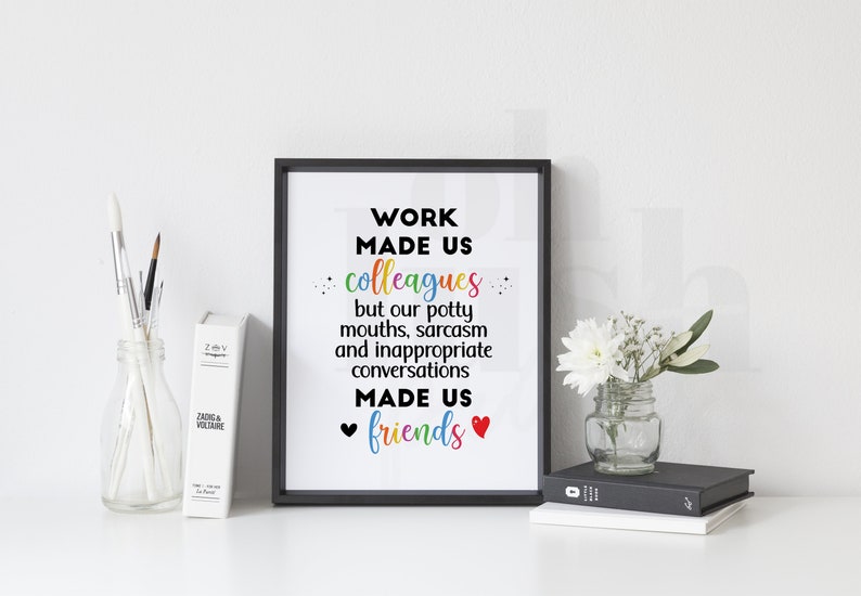 May include: A black framed print with a white background and the text "WORK MADE US colleagues but our potty mouths, sarcasm and inappropriate conversations MADE US friends" in black with rainbow colored letters. There are two red hearts at the bottom of the text.