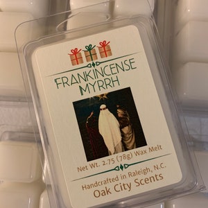 May include: A white wax melt with a label that reads "FRANKINCENSE MYRRH" and a picture of a person in a white robe. The label also includes the text "Net Wt. 2.75 (78g) Wax Melt", "Handcrafted in Raleigh, N.C.", and "Oak City Scents".